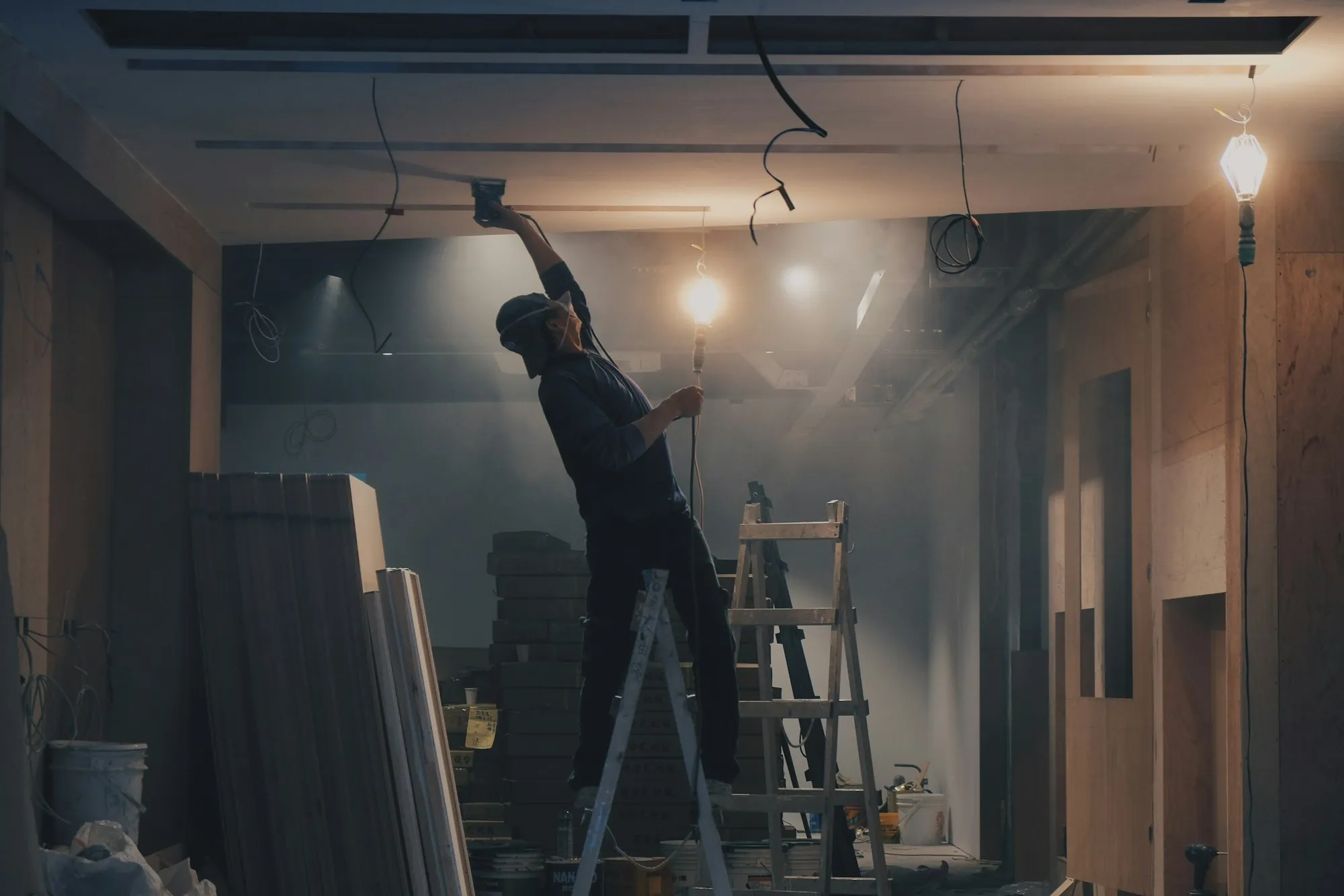Worker on a ladder fitting ceiling work in a framed room
