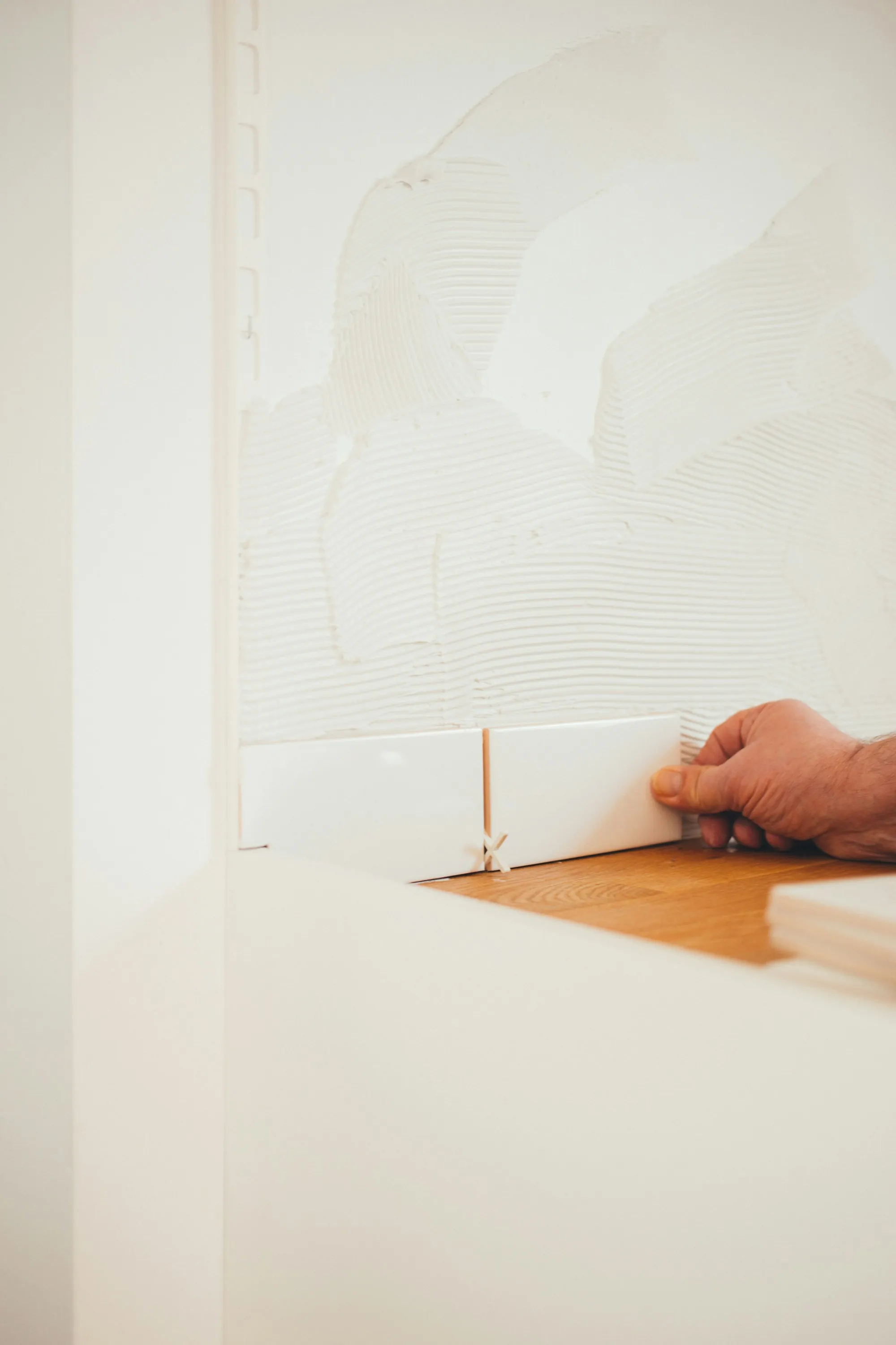 Installer pressing backsplash tile into fresh adhesive